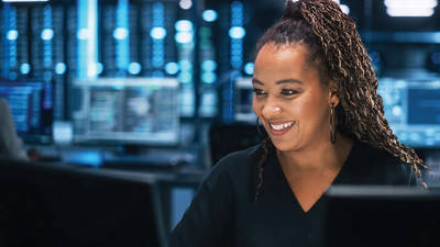 Black woman smiling and using a desktop computer in a data center