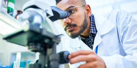 Indian male lab technician looking into a microscope