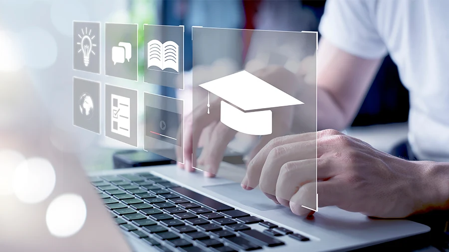 Close-up of hands typing on a laptop keyboard with projected square graphic icons of a graduate cap, lightbulb, text bubbles, and graphs.