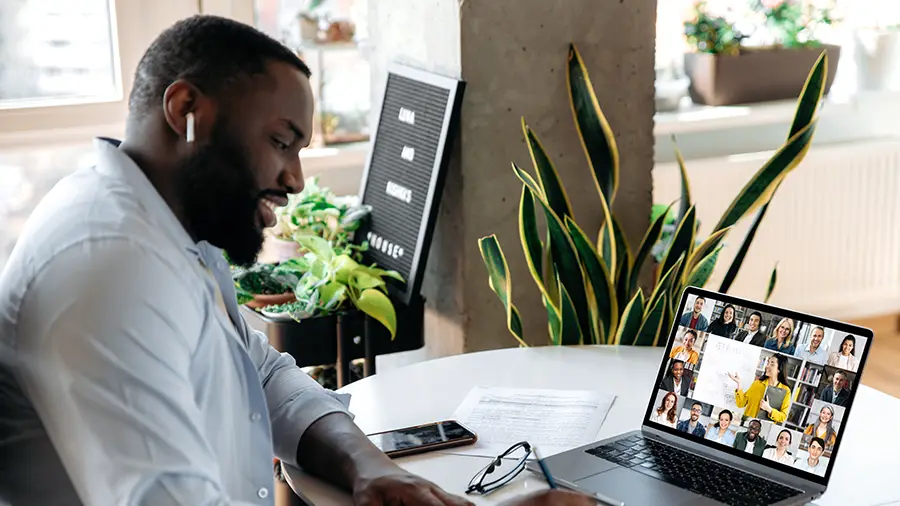 Black male Chick-fil-A®  Operator sitting at a desk using a laptop attending a virtual meeting with other Team Members. 
