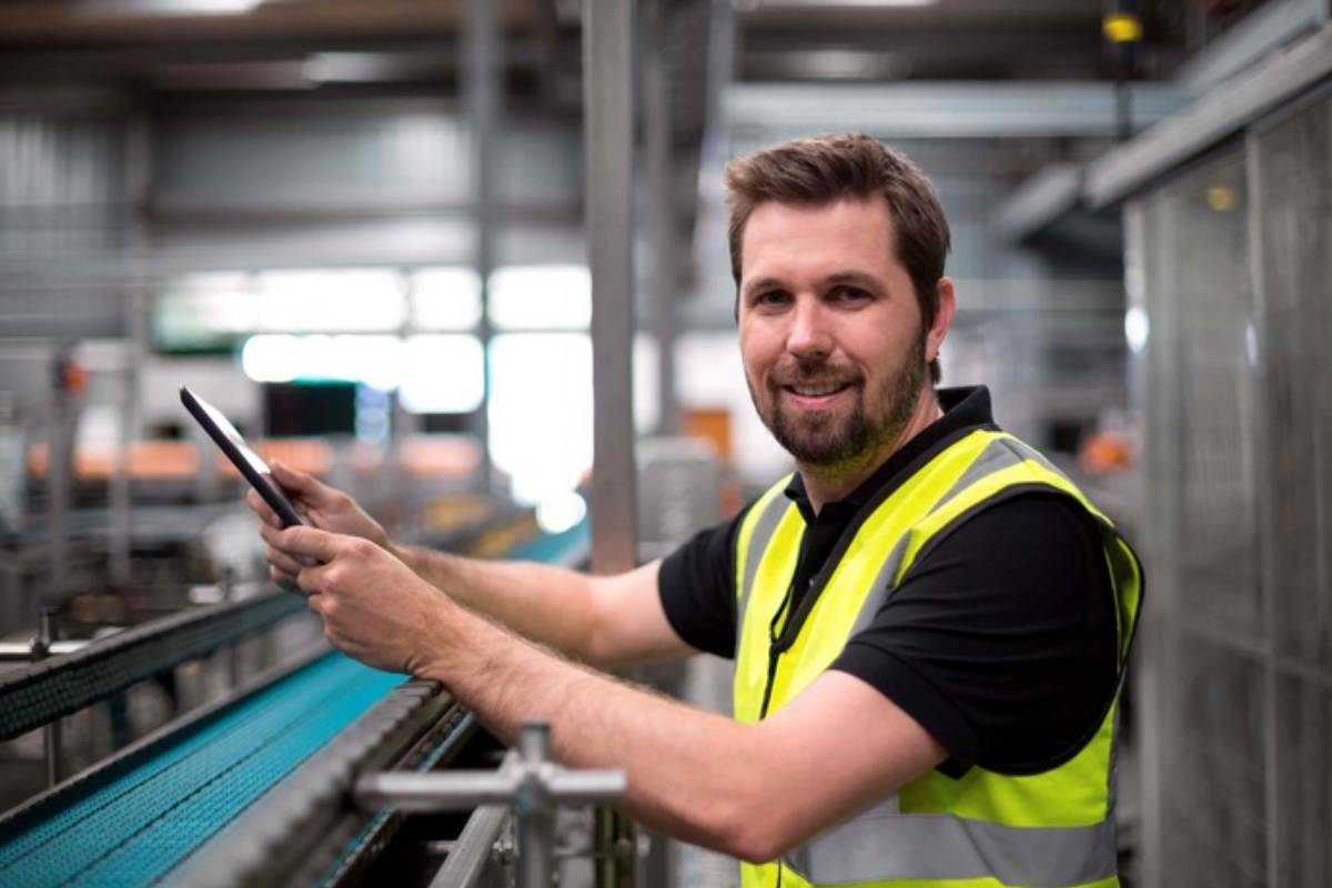 White male wearing a safety vest standing next to a manufacturing line in a warehouse
